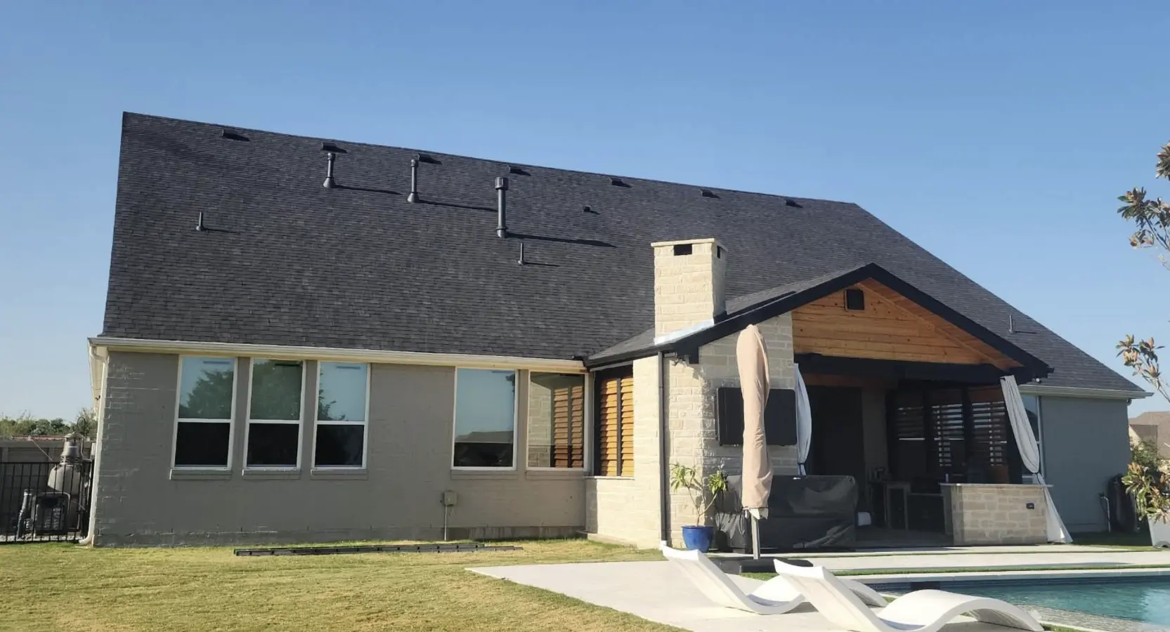 Completed residential roofing project in Bismarck, North Dakota, featuring a new dark asphalt shingle roof on a home with a chimney and pool area by Bismarck Exterior Pros.