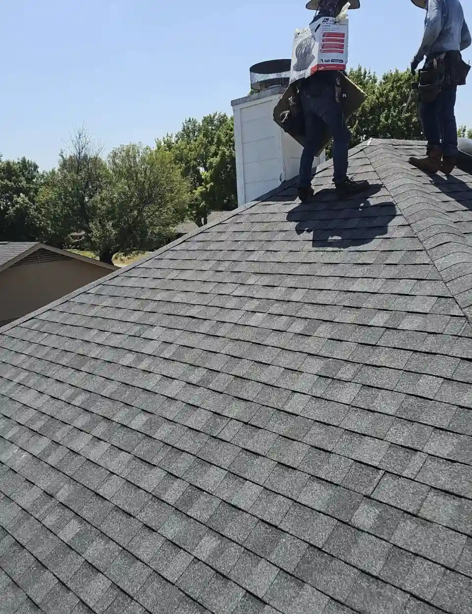 Bismarck, North Dakota roofing contractors installing new grey asphalt shingles around a chimney during a roof replacement by Bismarck Exterior Pros.