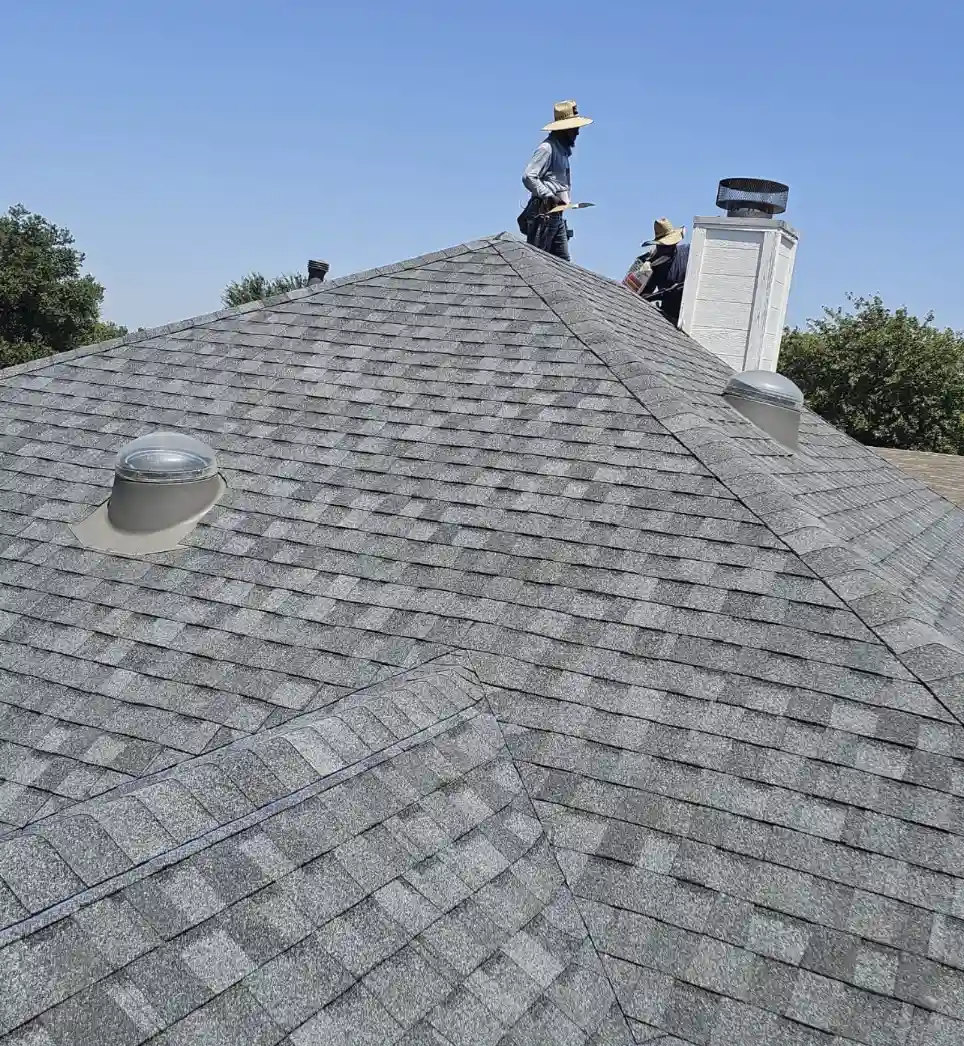 Bismarck, North Dakota roofing contractors installing new grey asphalt shingles and chimney flashing during a roof replacement by Bismarck Exterior Pros.