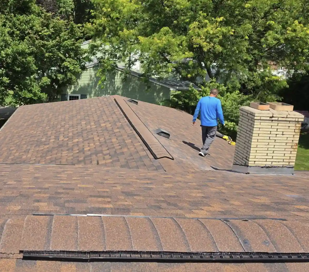Bismarck, North Dakota roofing contractor inspecting a completed roof replacement with new brown asphalt shingles, ridge vents, and chimney flashing by Bismarck Exterior Pros.